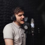 man sings into microphone, professional recording studio, headphones. Black soft walls, sound insulation. singer records his song.